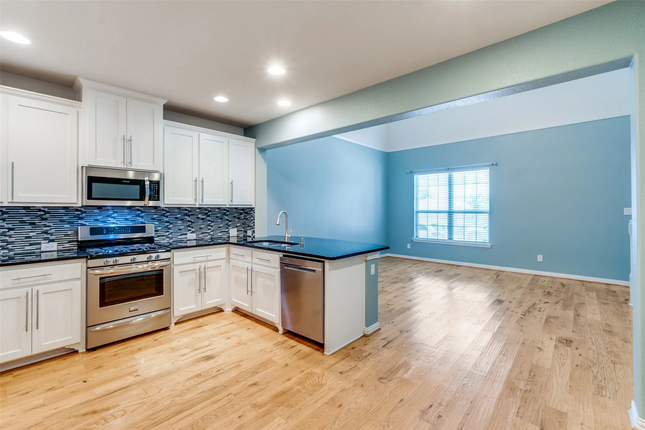 Kitchen featuring stainless steel appliances, backsplash, a peninsula, light wood-style floors, and recessed lighting