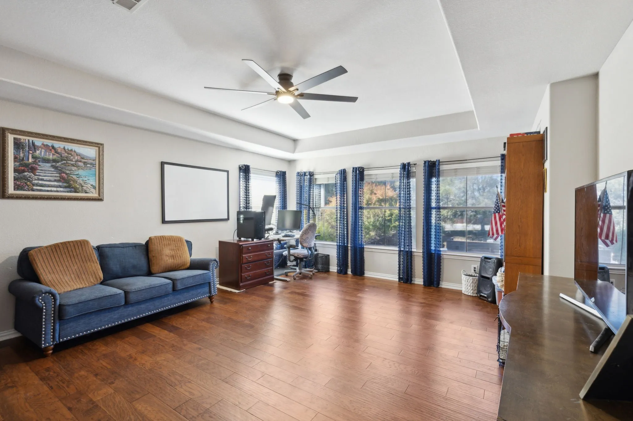 Game room on the second floor has tray ceiling, ceiling fan and wood flooring.
