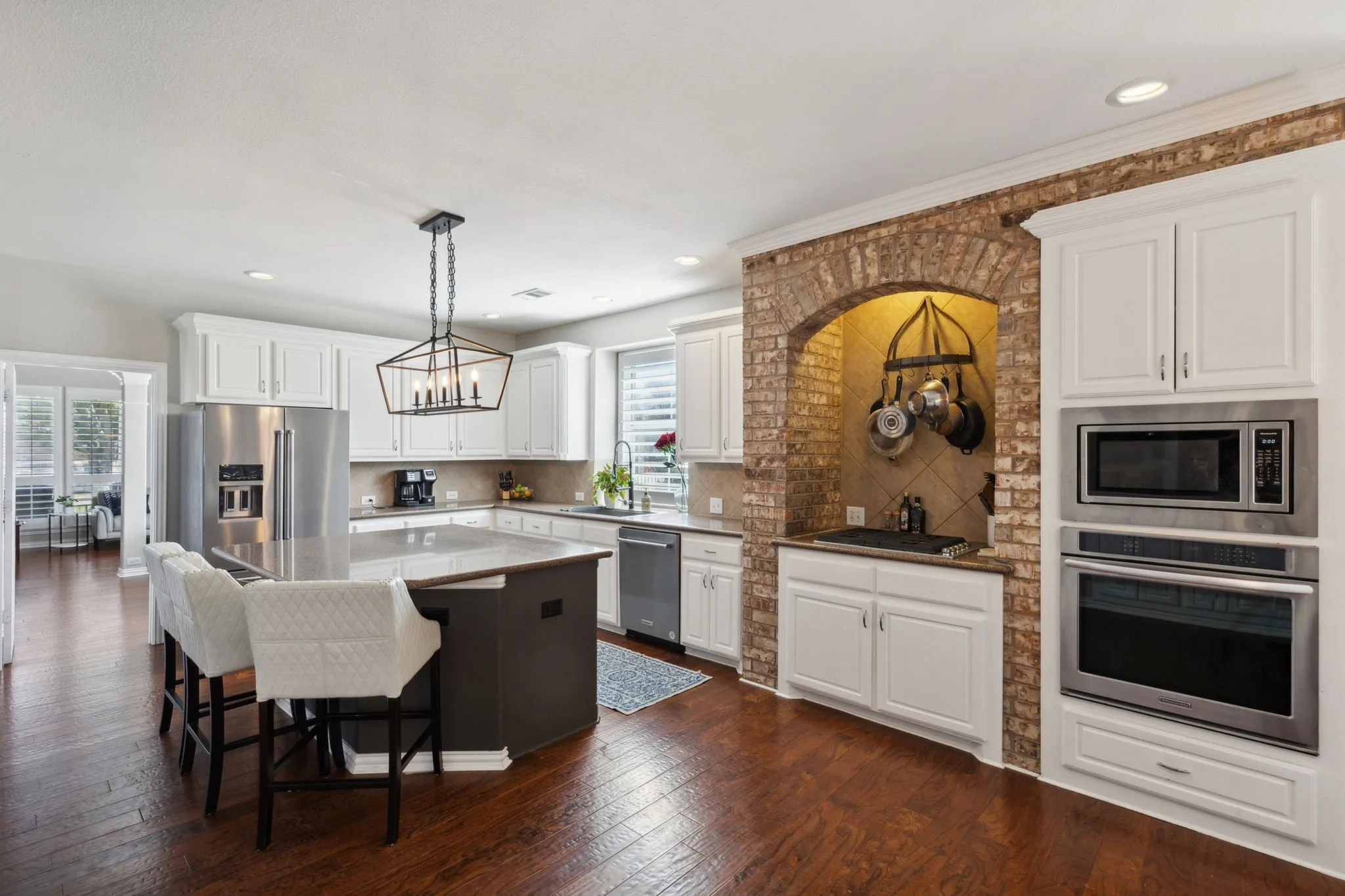 Brick alcove with 4 burner gas cooktop adds a Tuscan flair to this striking kitchen. Stainless oven and microwave are nearby.