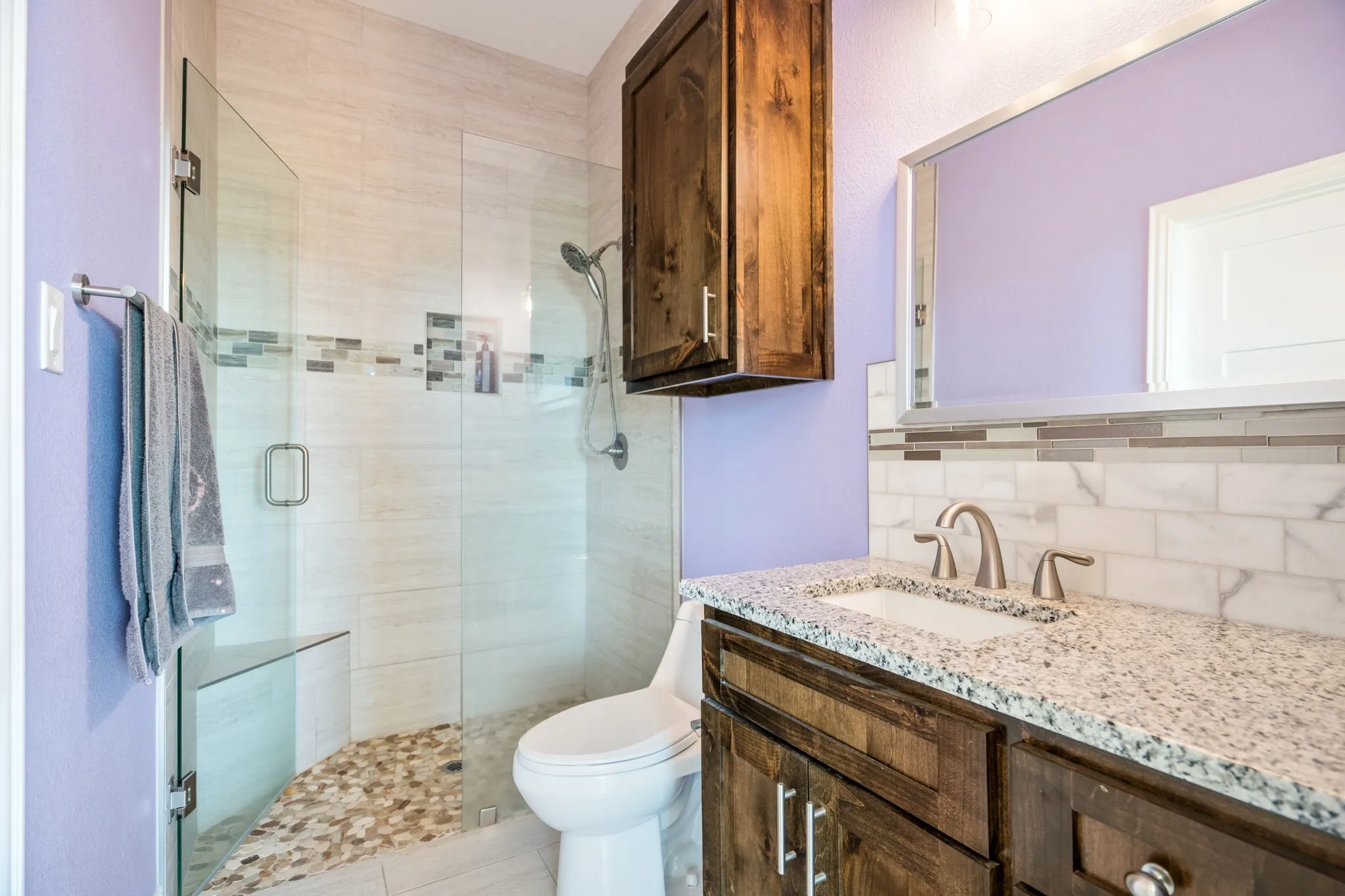 Glass-enclosed shower with a built-in bench, pebble floor, and tiled walls with decorative mosaic accents