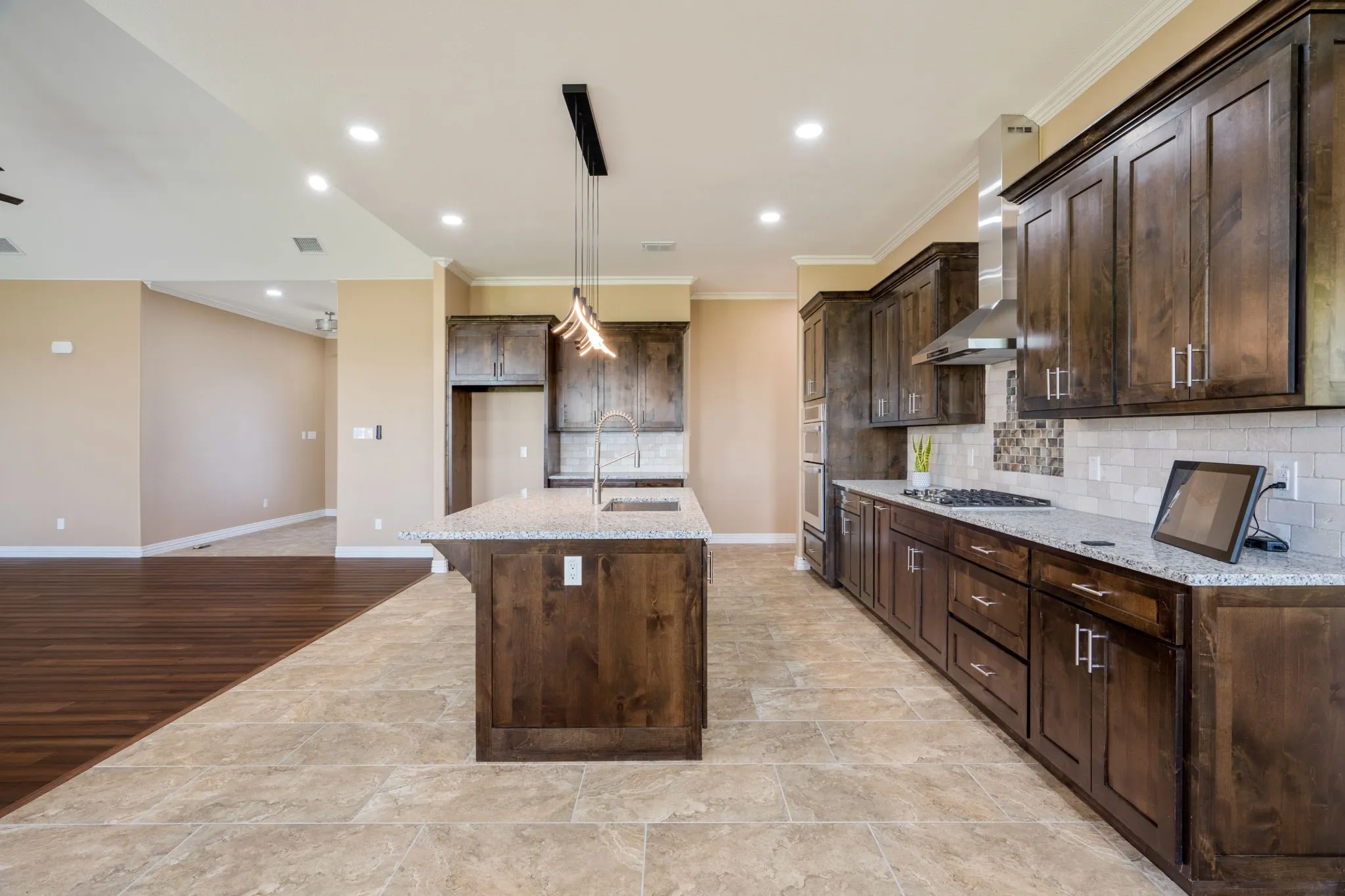 Spacious kitchen featuring an island with a built-in sink, dark wood cabinetry, light granite countertops, a tiled backsplash, and recessed lighting