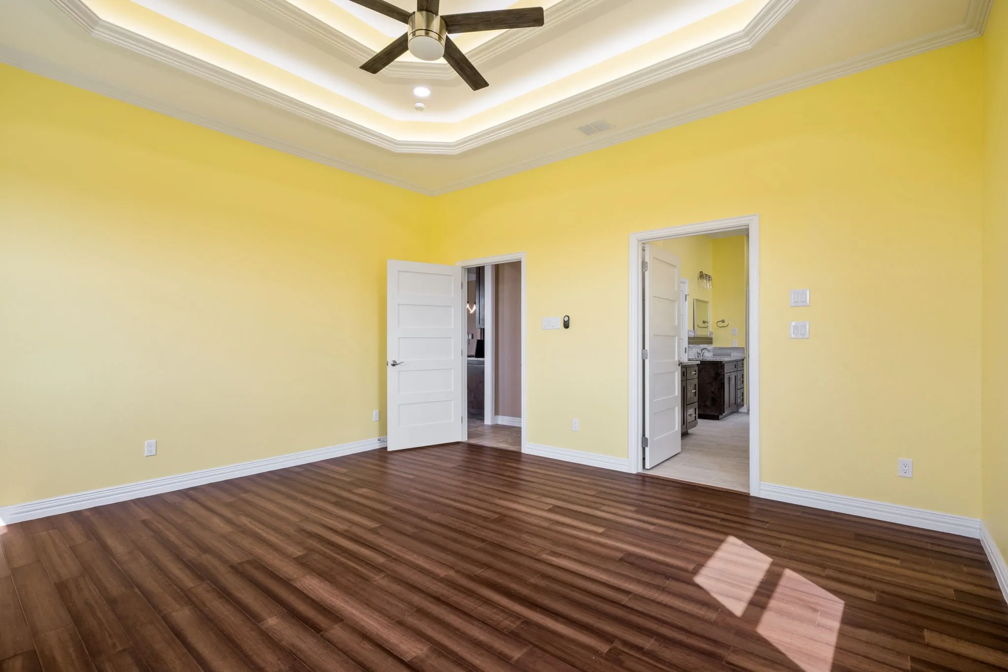 Spacious room featuring wood-finish flooring, a tray ceiling with recessed lighting, and a ceiling fan
