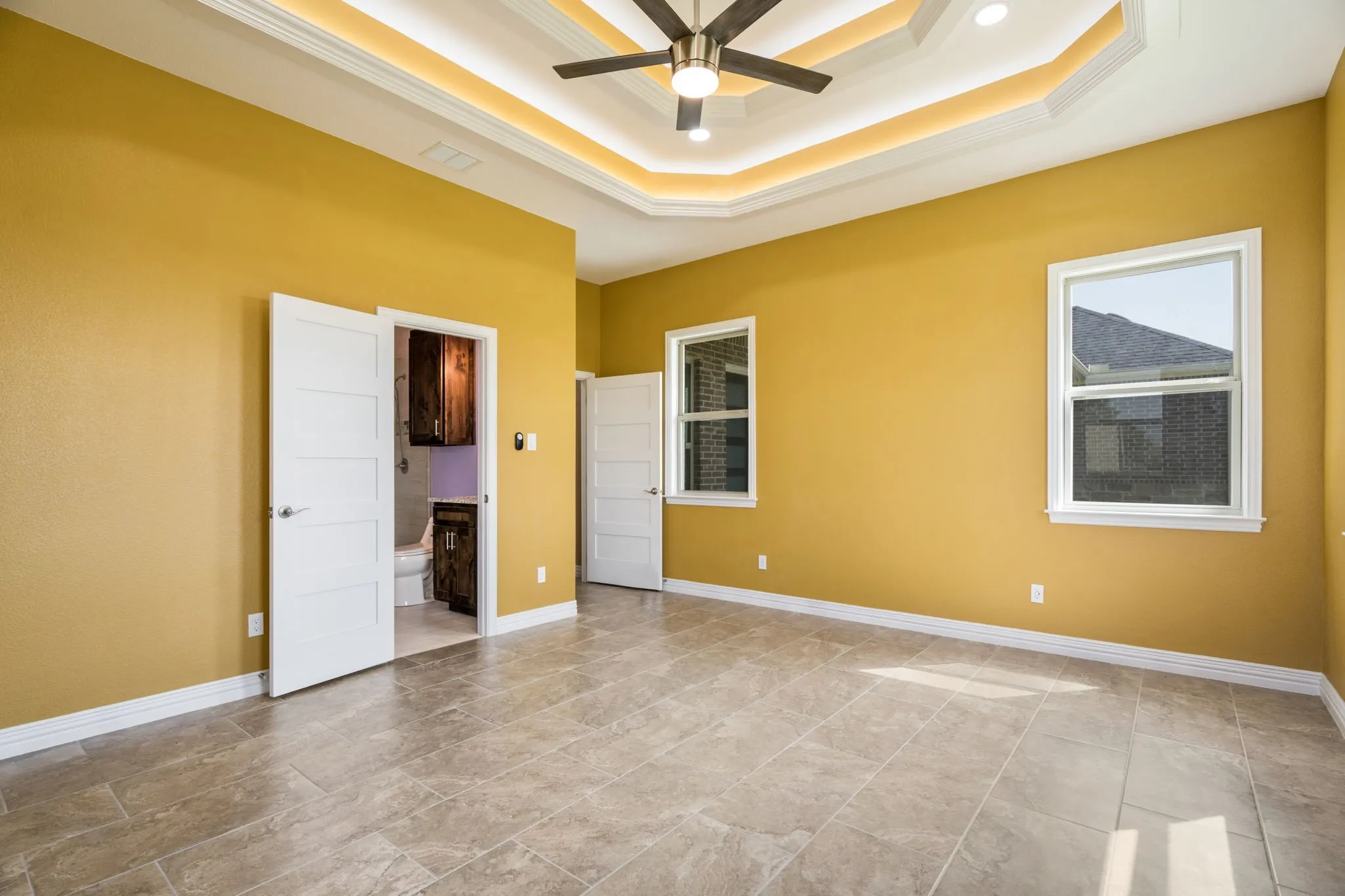 Spacious room featuring tile flooring, two windows, and a multi-tiered tray ceiling with recessed lighting and a ceiling fan
