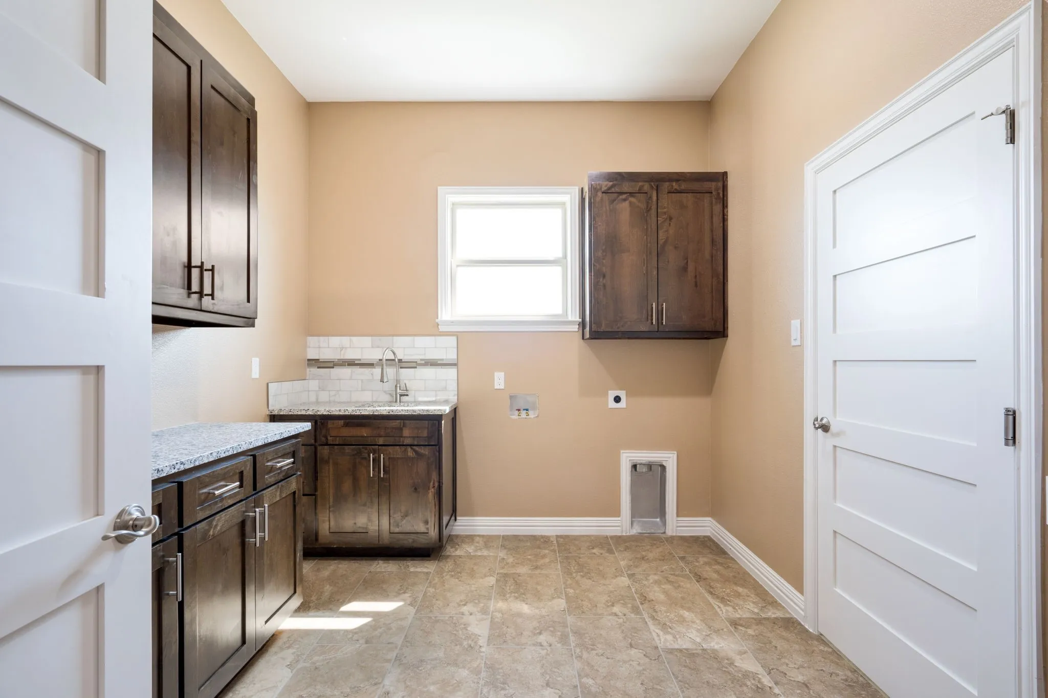 Utility room featuring wood-finish cabinetry, granite countertops, an undermount sink with a gooseneck faucet, a subway tile backsplash, and tile flooring