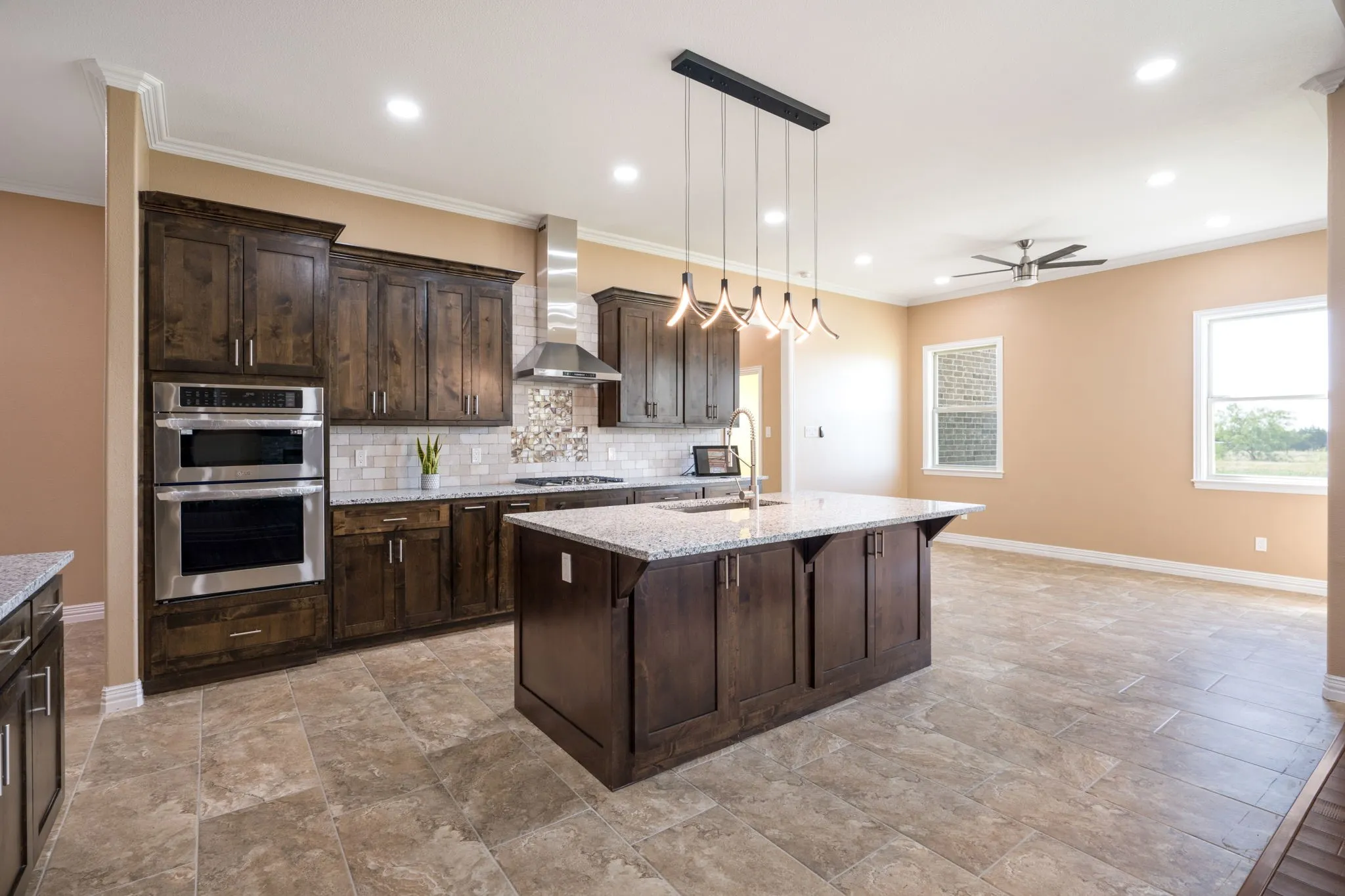 Contemporary kitchen featuring dark wood cabinetry, stainless steel appliances, a large center island with a granite countertop, a tile backsplash, and recessed lighting