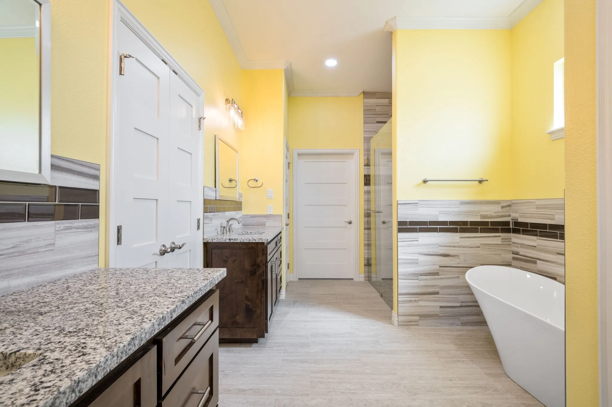 Spacious bathroom featuring a freestanding soaking tub, a glass-enclosed shower, dual vanity with granite countertops, wood-finish cabinetry, and tiled flooring