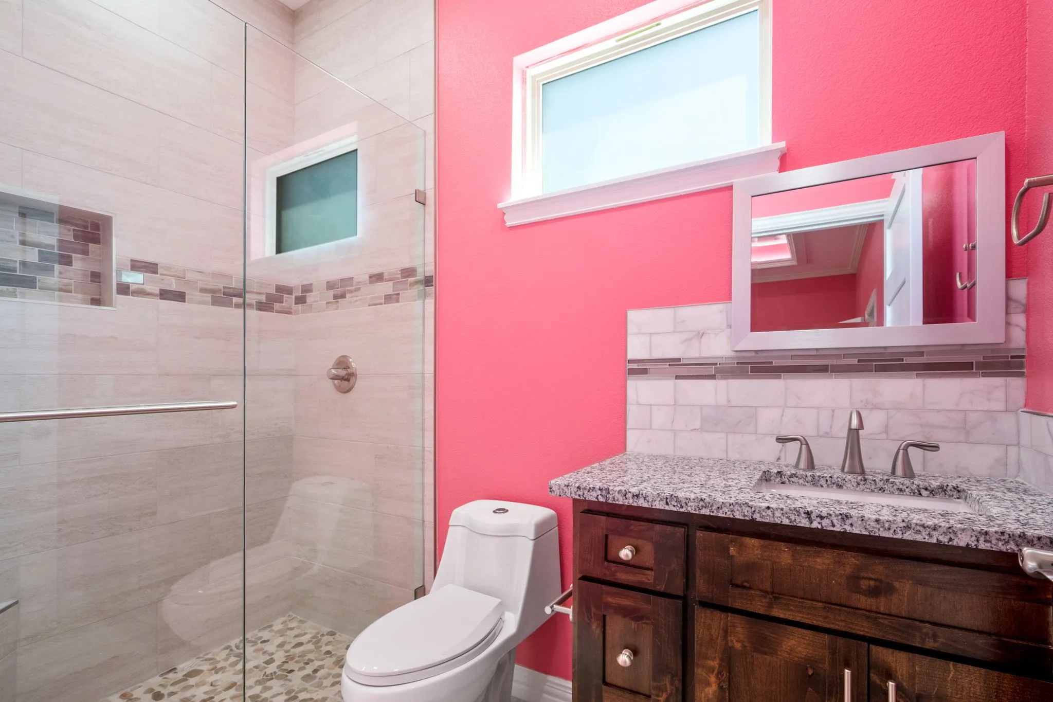 Glass-enclosed shower with pebbled floor, tiled walls, and built-in niche