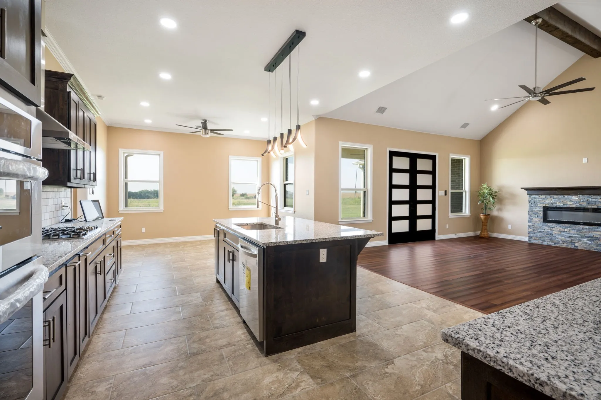 Open-concept kitchen and living area featuring a vaulted ceiling with exposed beams, recessed lighting, and ceiling fans