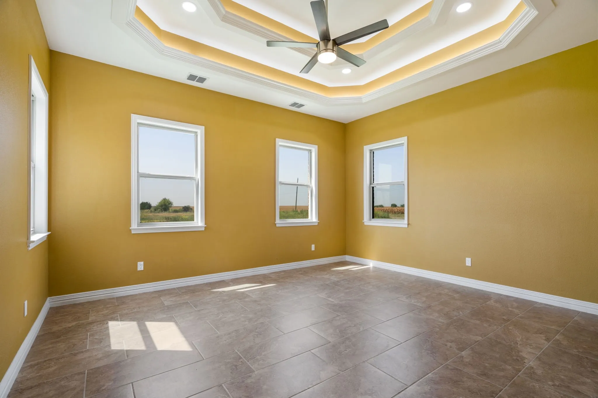 Spacious room featuring a multi-tiered tray ceiling with recessed lighting and a ceiling fan