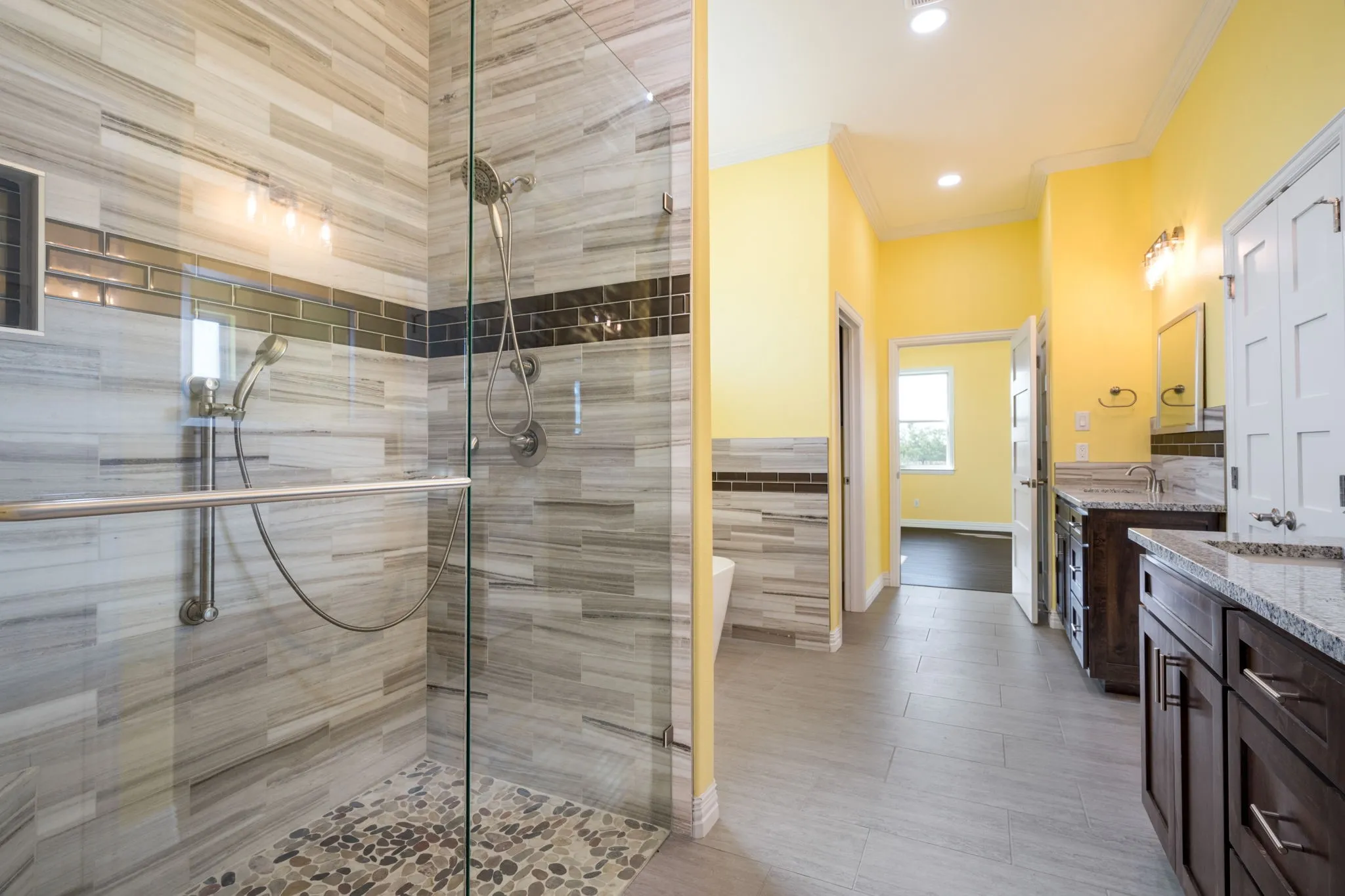 Spacious bathroom featuring a glass-enclosed shower with pebble flooring and a tiled accent band