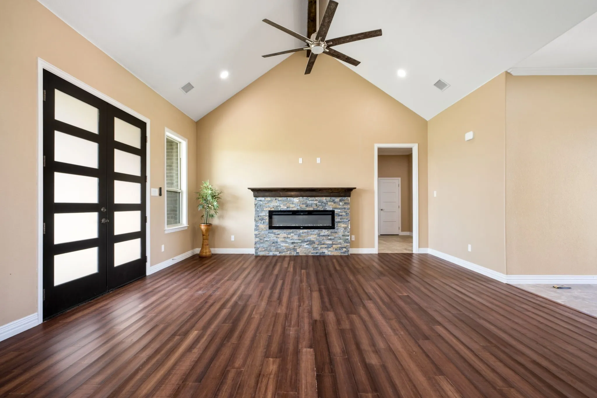 Vaulted living area featuring rich wood-finish flooring, a modern linear fireplace with stone surround, and a stylish ceiling fan