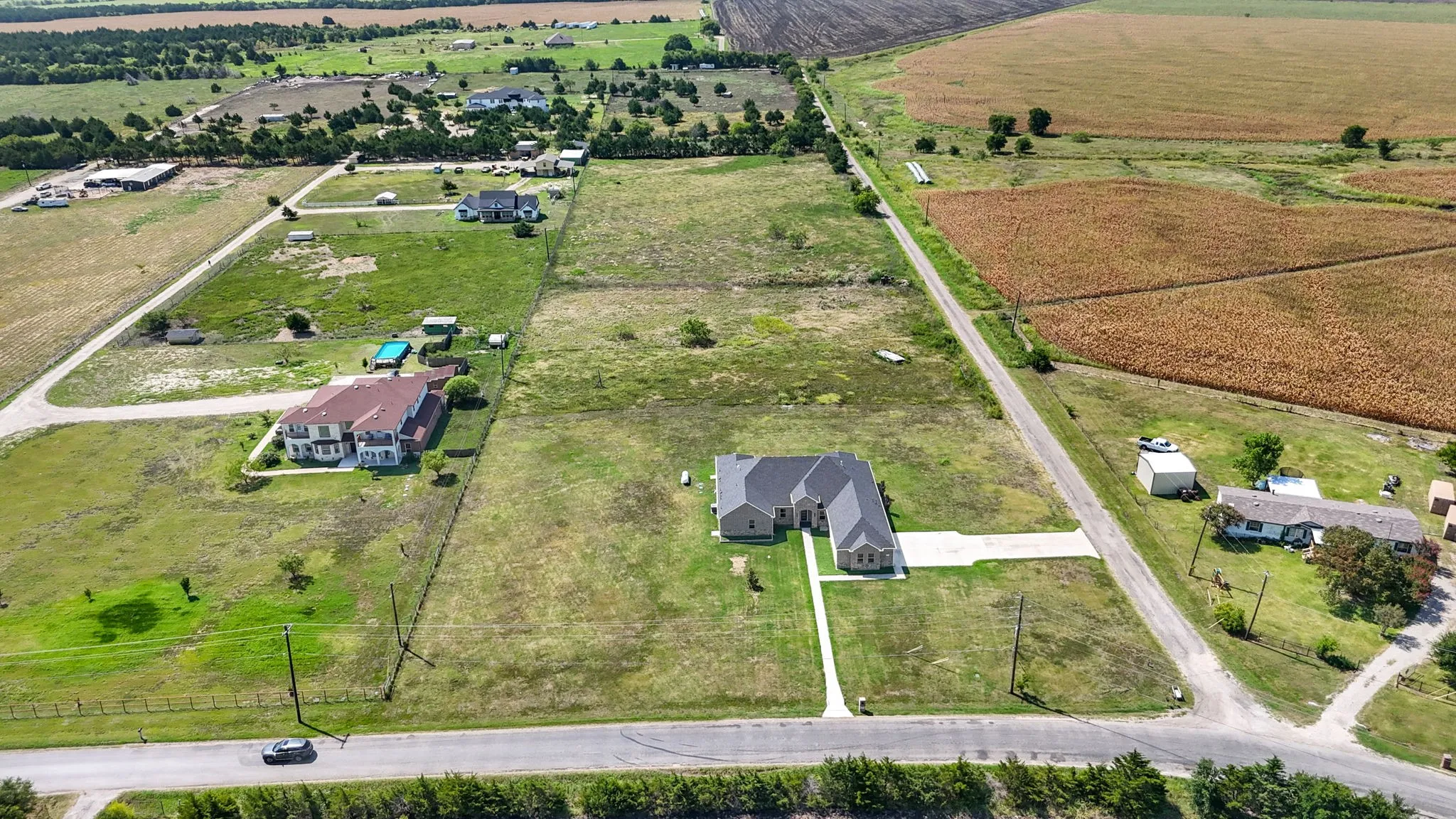 Expansive rural property featuring a single-story residence with a light gray exterior and a dark gray roof