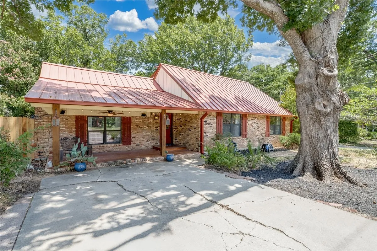 Brick exterior with a standing seam metal roof, covered front porch, and mature​​‌​​​​‌​​‌‌​‌‌​​​‌‌​‌​‌​‌​​​‌​​ trees