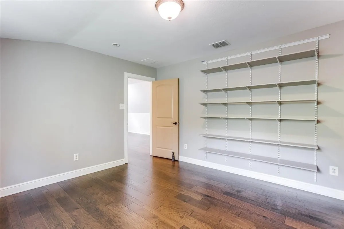 Room featuring wood-finish flooring, light grey walls, and extensive built-in shelving