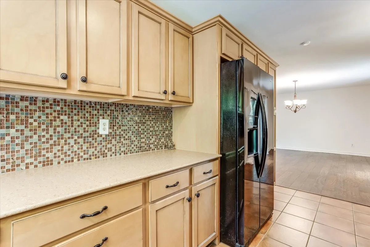 Kitchen featuring light wood cabinetry with dark hardware, a mosaic tile backsplash, light-toned countertops, and a black side-by-side refrigerator