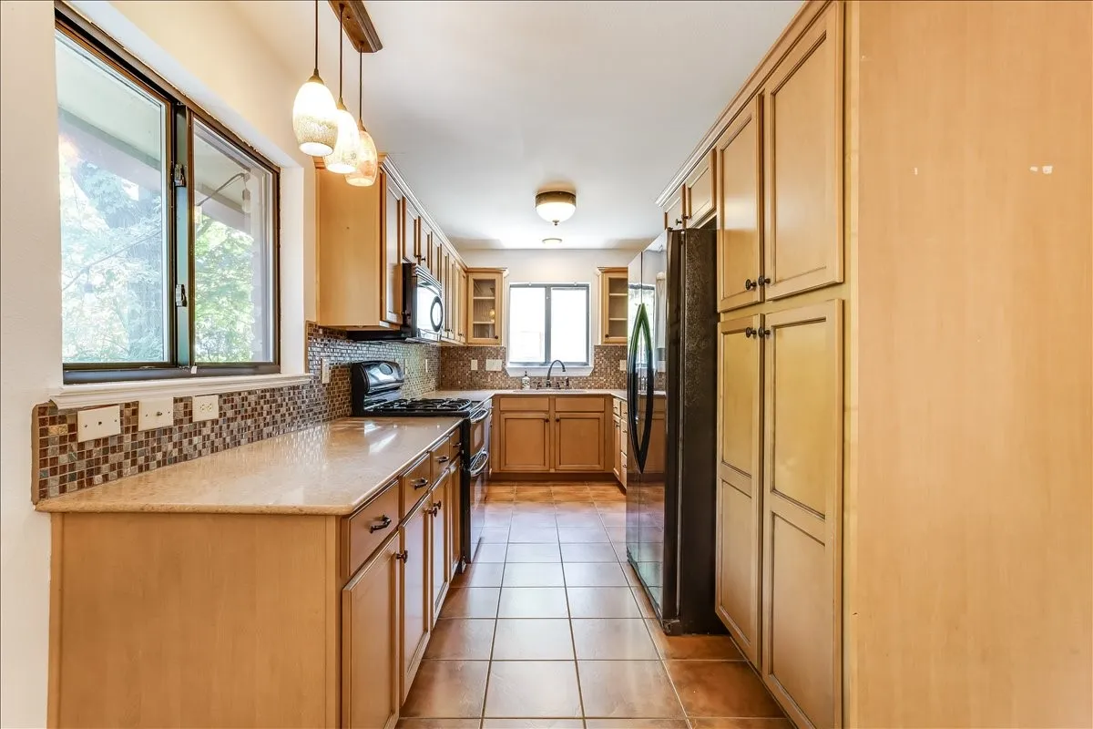Galley kitchen with light wood-finish cabinetry, tile flooring, and granite-style countertops