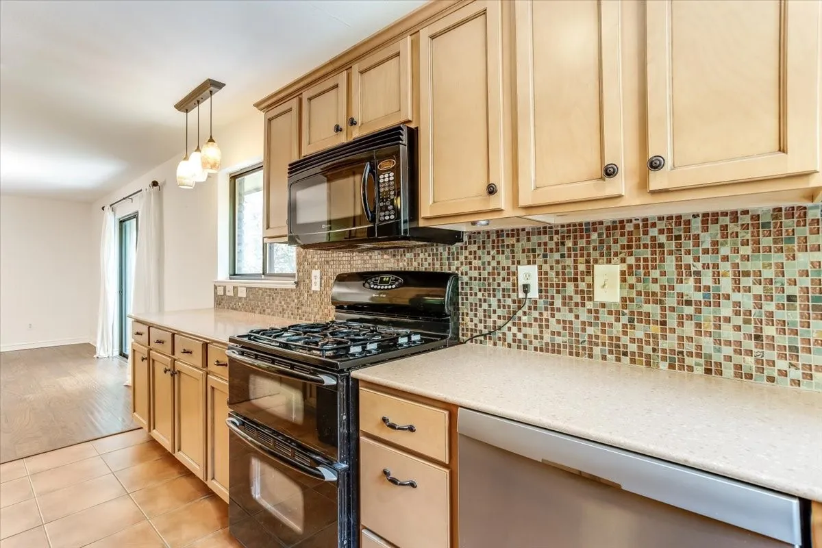 Kitchen featuring light wood cabinetry, a mosaic tile backsplash, black gas range with a double oven, black built-in microwave, and a counter-depth dishwasher