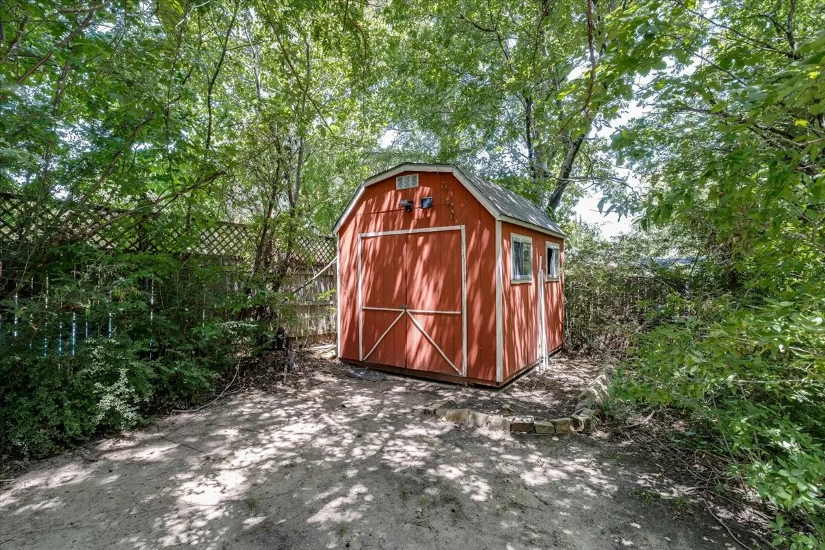 Freestanding red storage shed featuring a gable roof, double barn doors, and two windows