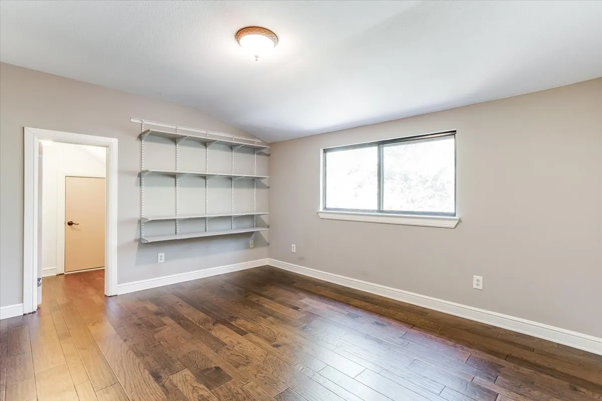 Room featuring wood-finish flooring, a vaulted ceiling, and built-in shelving