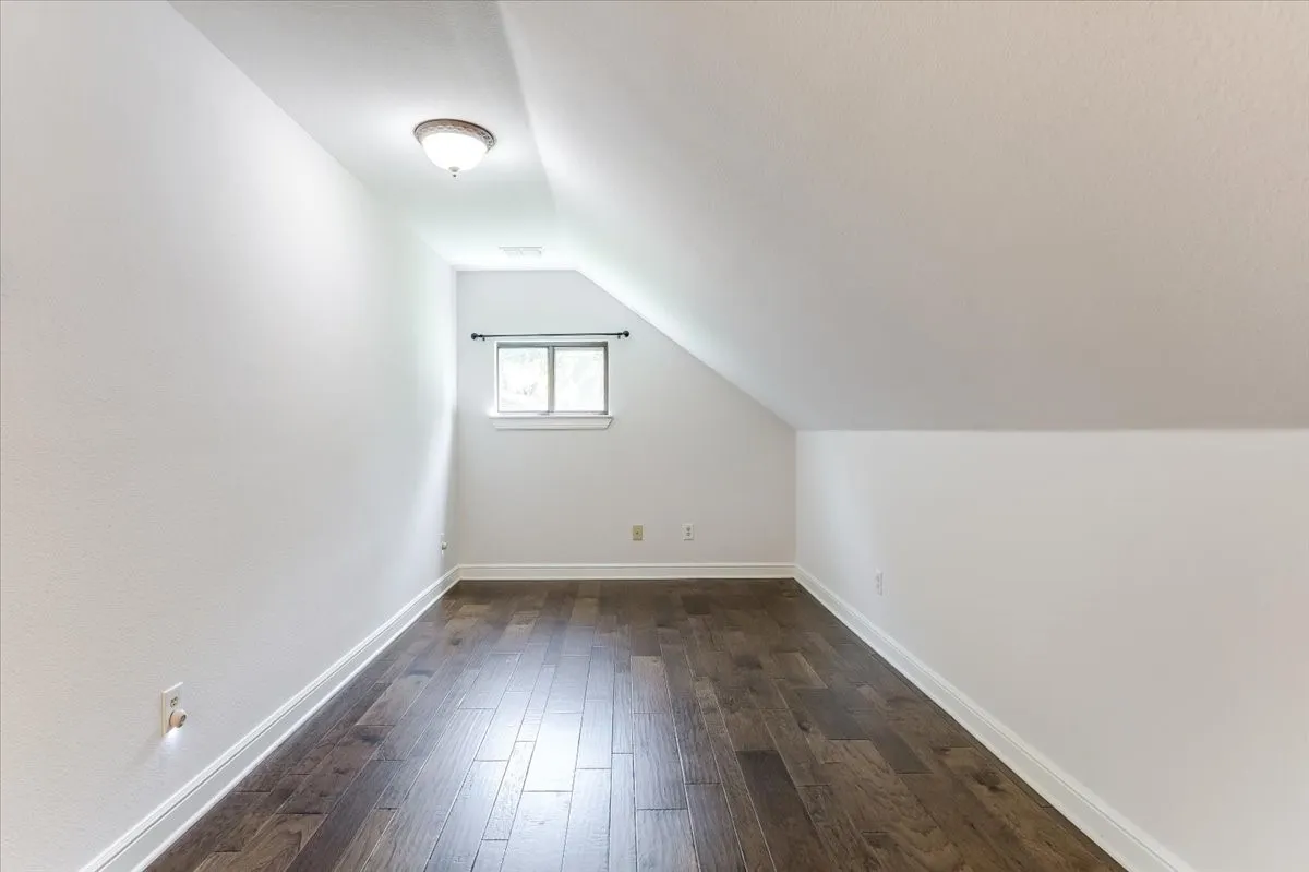 Attic room featuring wood-finish flooring, a window with natural light, and a ceiling-mounted light fixture