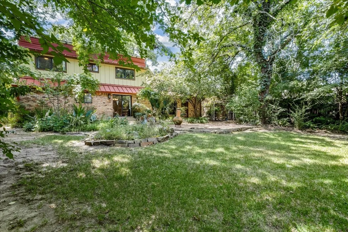 Expansive backyard featuring a manicured lawn, mature trees, and a stone patio
