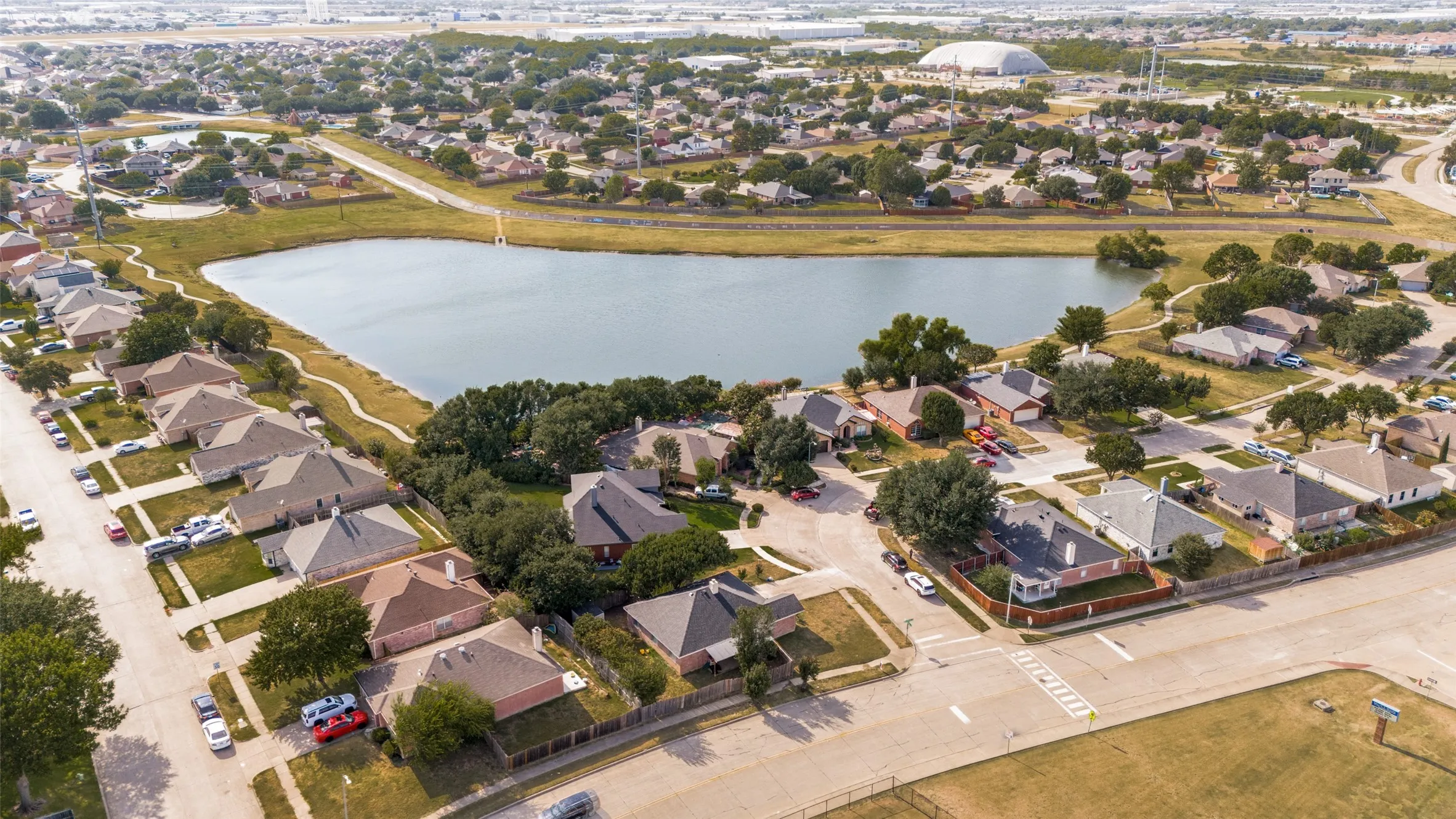Residential neighborhood featuring a pond, mature trees, and paved roads