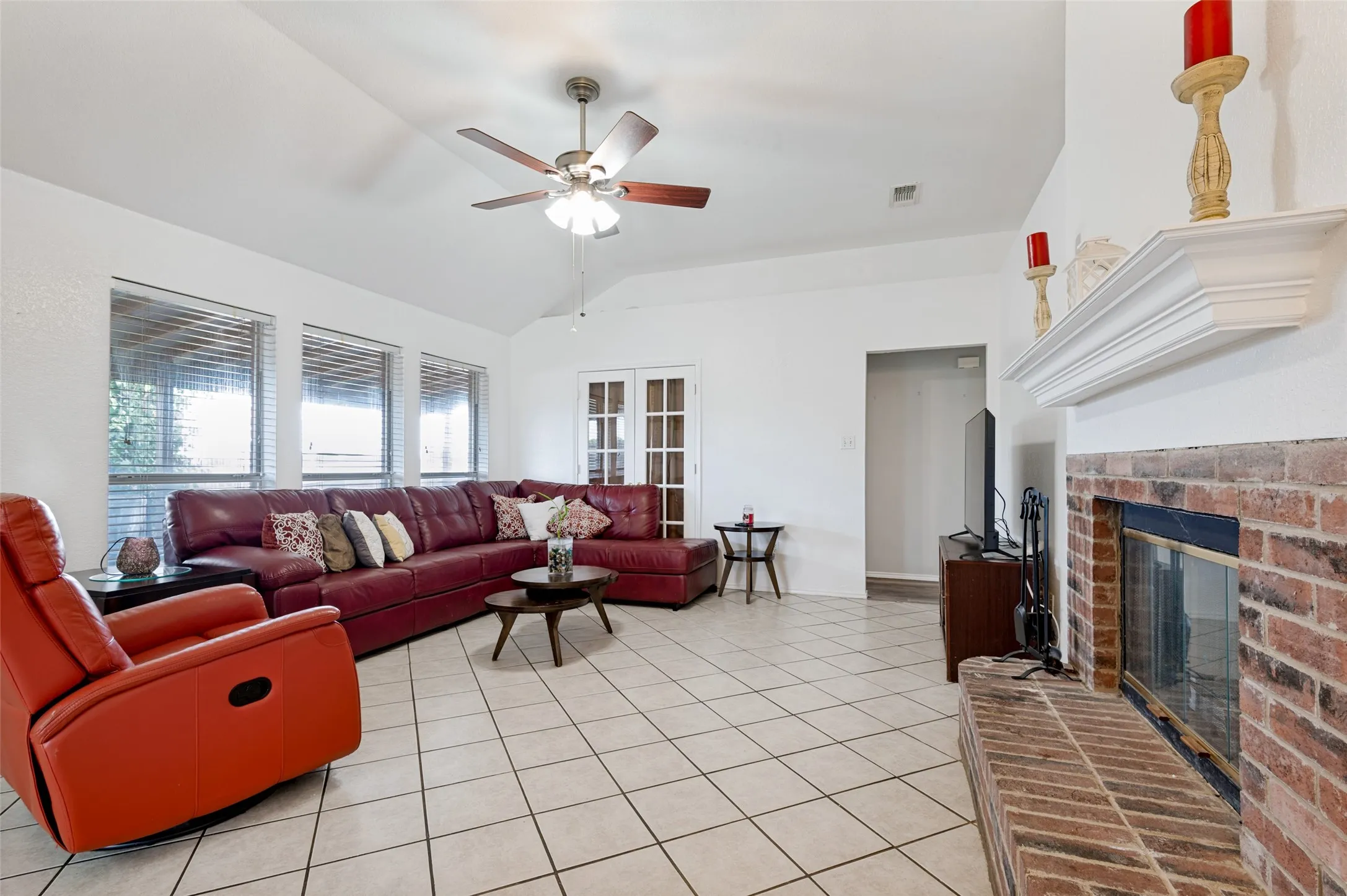 Vaulted ceiling, ceiling fan, multiple windows, brick fireplace with mantel, and tile flooring