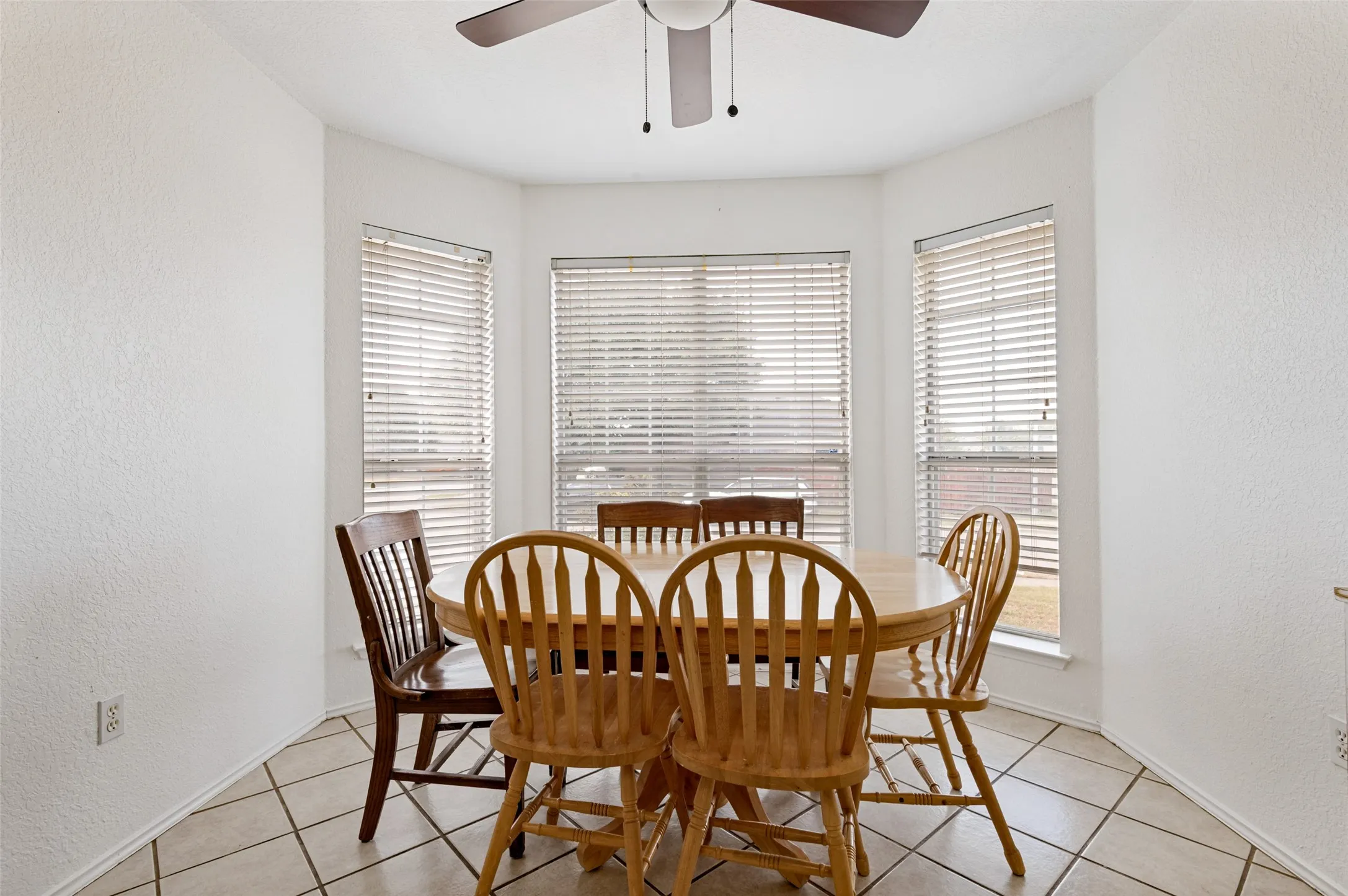 Bay window with multiple windows, tile flooring, and ceiling fan