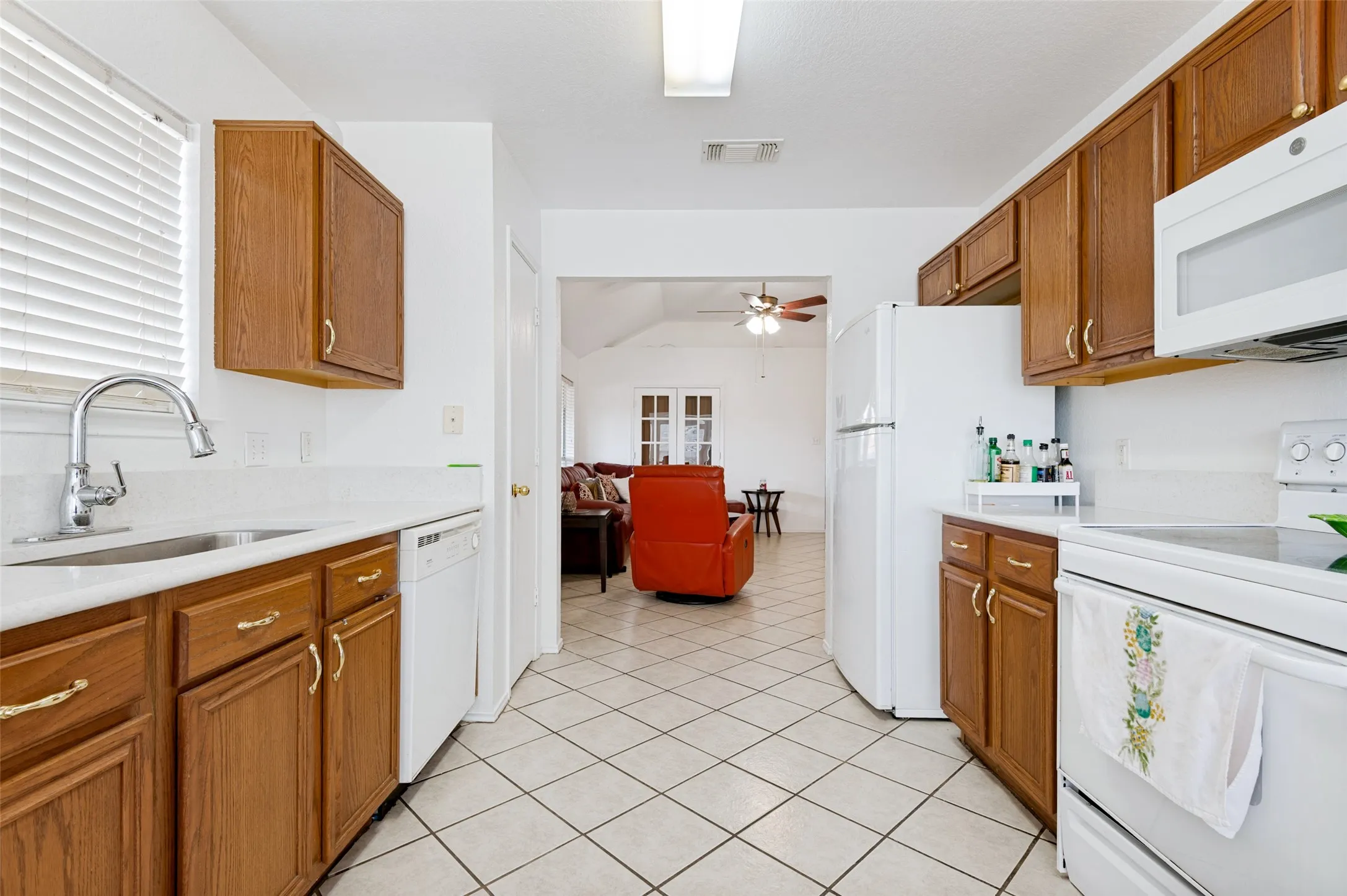 Kitchen featuring wood-finish cabinetry, white countertops, a stainless steel sink with a gooseneck faucet, white appliances, and tiled flooring