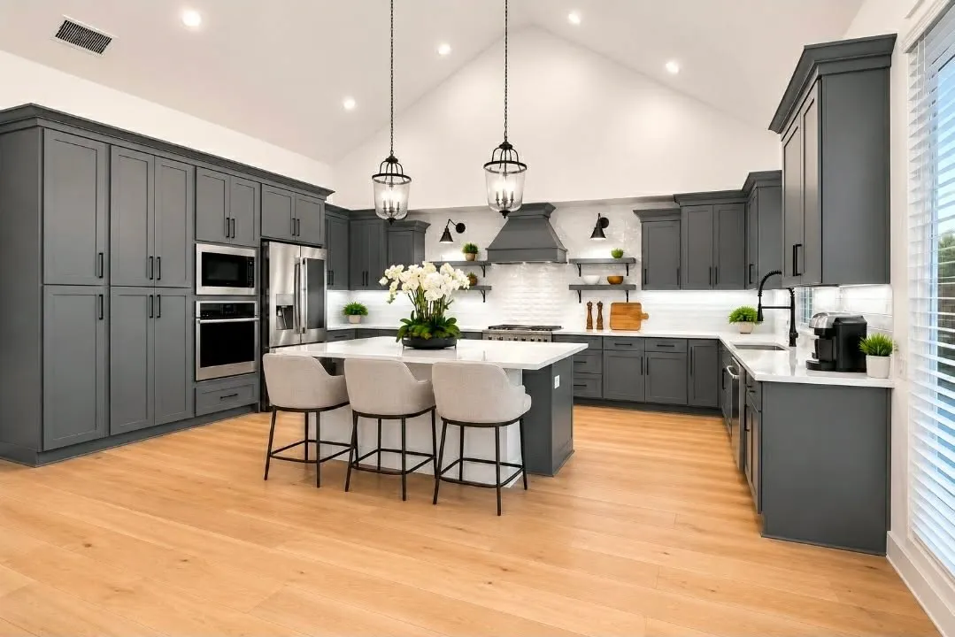 Expansive kitchen featuring a large central island with seating, dark shaker-style cabinetry, wood-finish flooring, stainless steel appliances, and a vaulted ceiling with recessed lighting