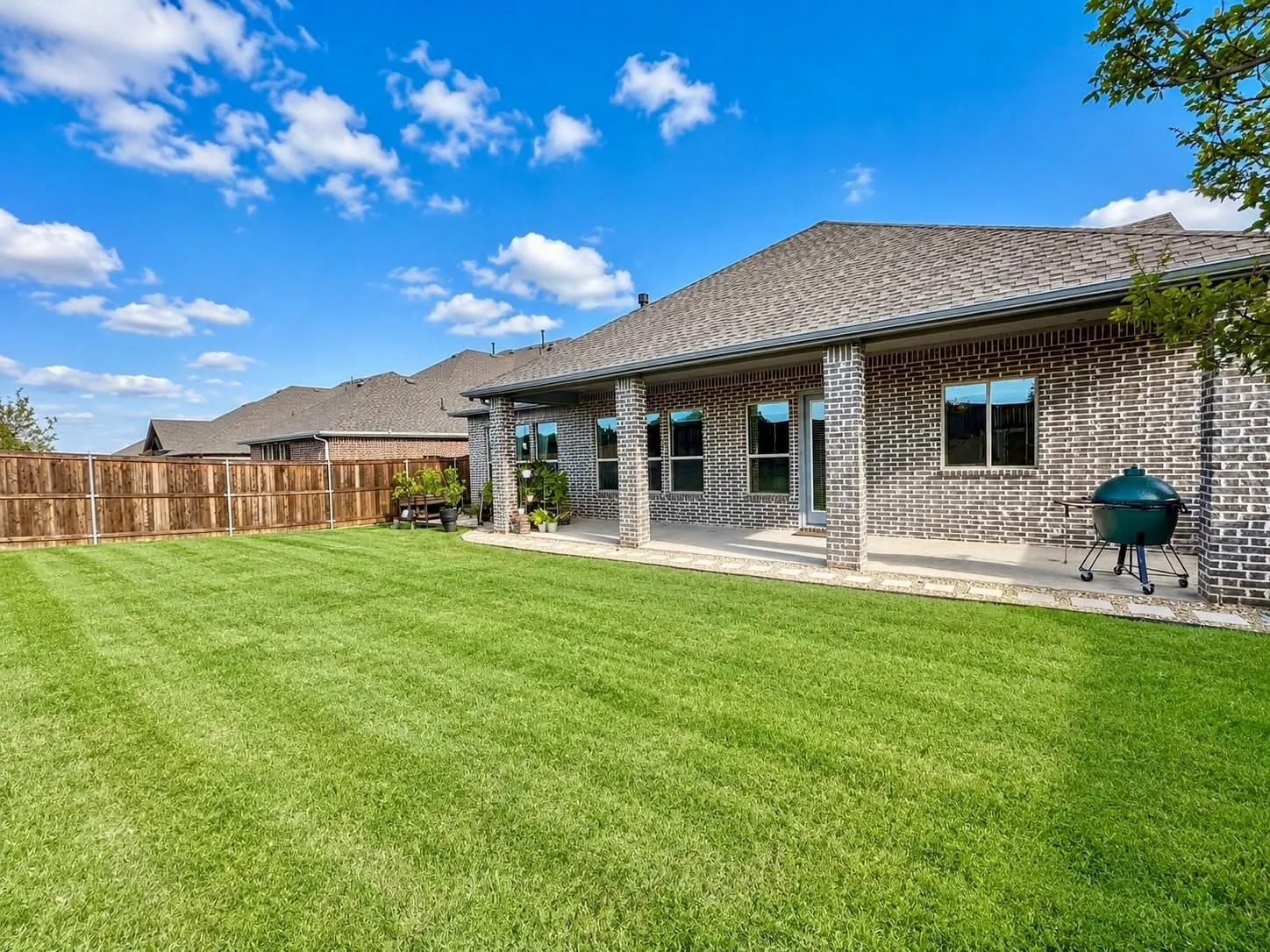 Expansive backyard featuring a manicured lawn, wood privacy fencing, and a covered concrete patio
