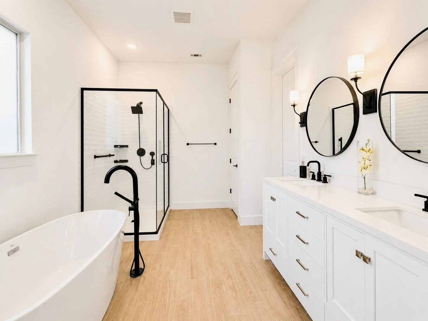 Modern bathroom featuring a freestanding soaking tub with a matte black floor-mounted faucet, a walk-in shower with black-framed glass enclosure, and a double vanity with white cabinetry and integrated sinks