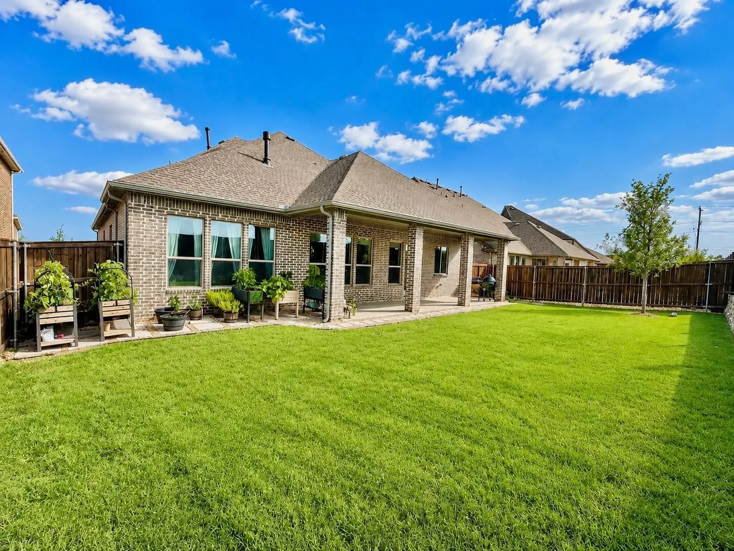 Spacious backyard featuring a large green lawn, a covered patio, and a privacy fence