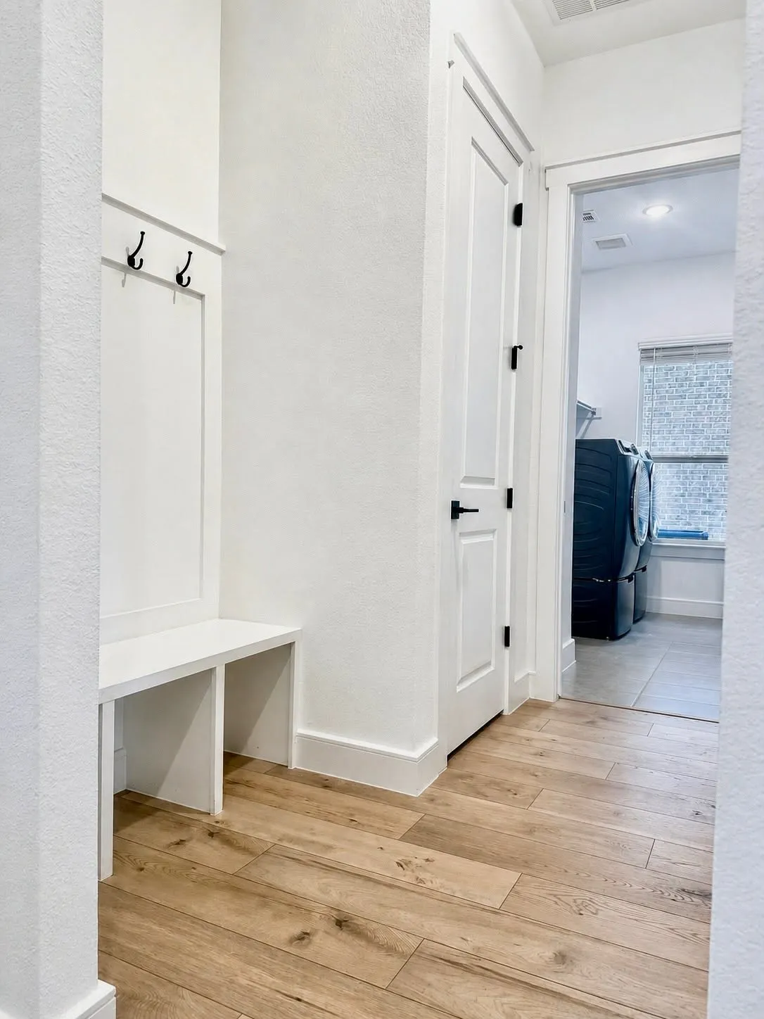 Entryway mudroom featuring built-in bench seating and coat hooks, wood-finish flooring, and white trim