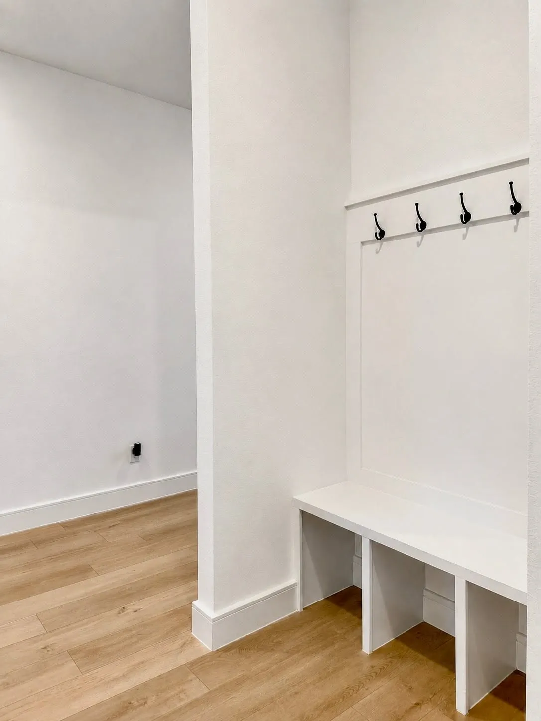 Built-in mudroom bench with three cubby compartments, a paneled back wall, and four matte black coat hooks