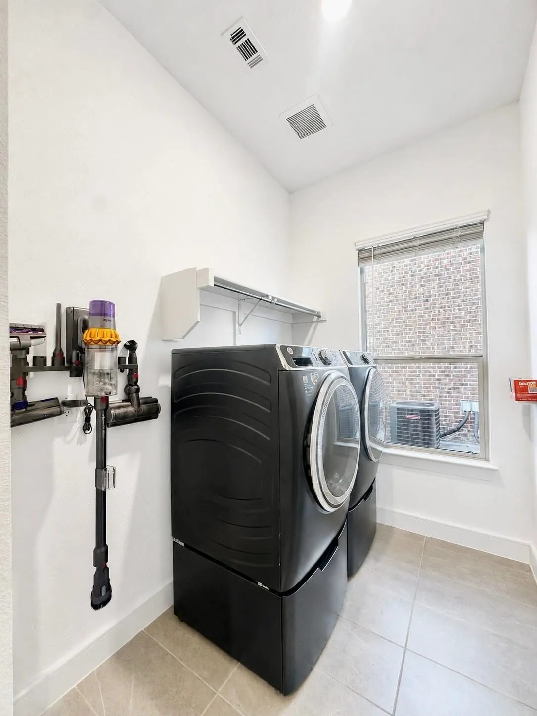 Laundry area featuring light-toned tile flooring, white walls, and a window with blinds