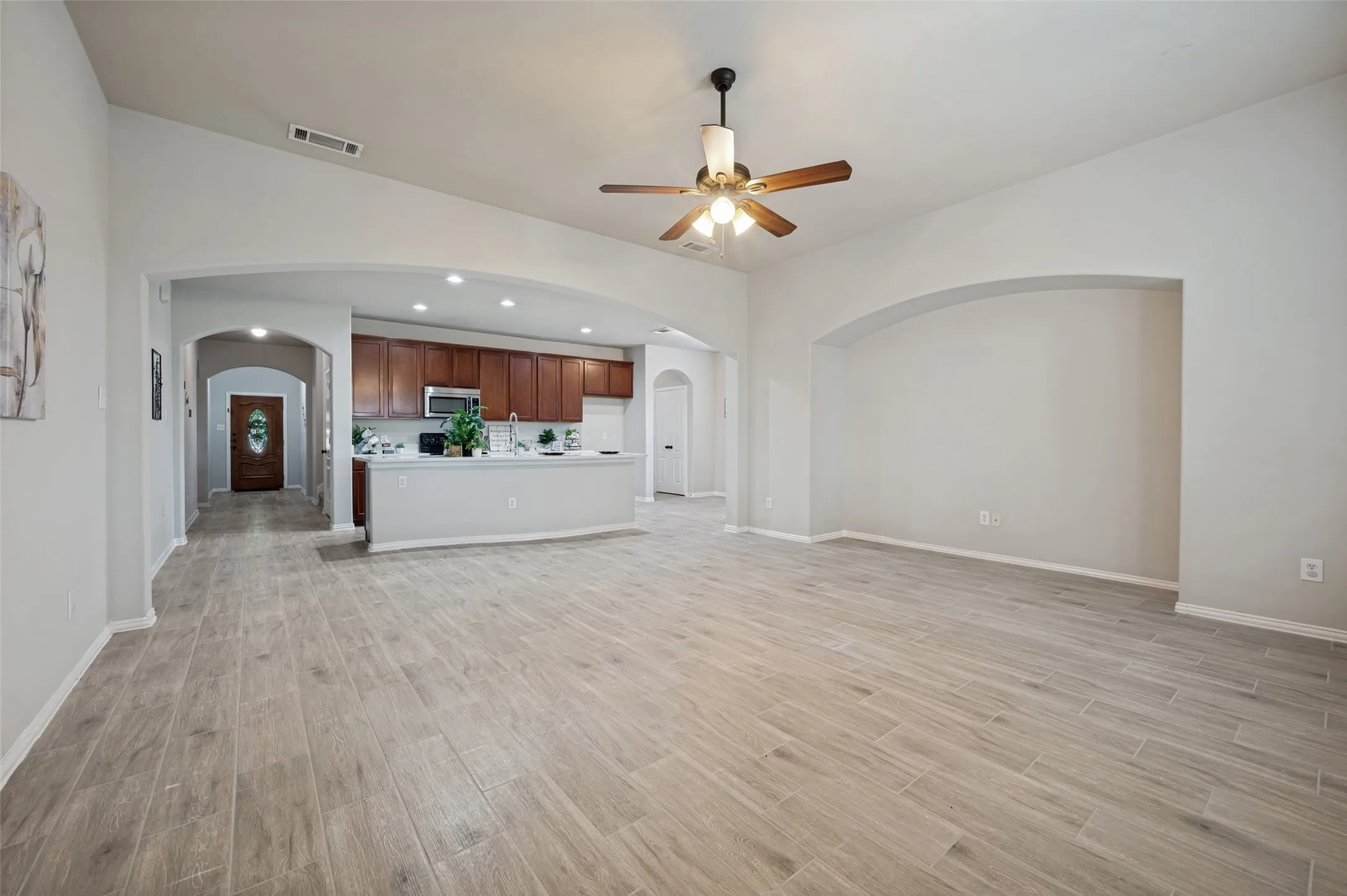 Spacious open-concept interior featuring light wood-finish flooring, high vaulted ceilings, and a ceiling fan