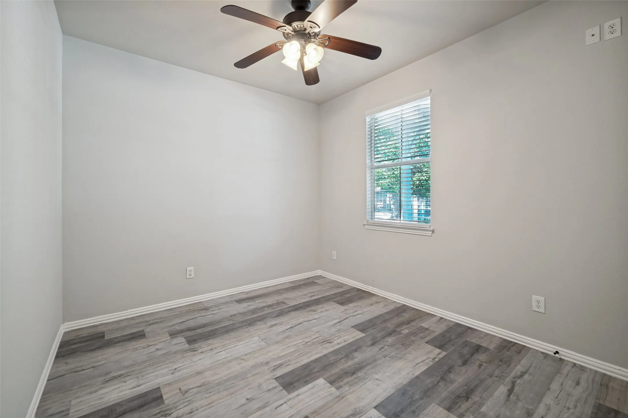 Room featuring wood-finish flooring, a ceiling fan with integrated lighting, and a window with blinds