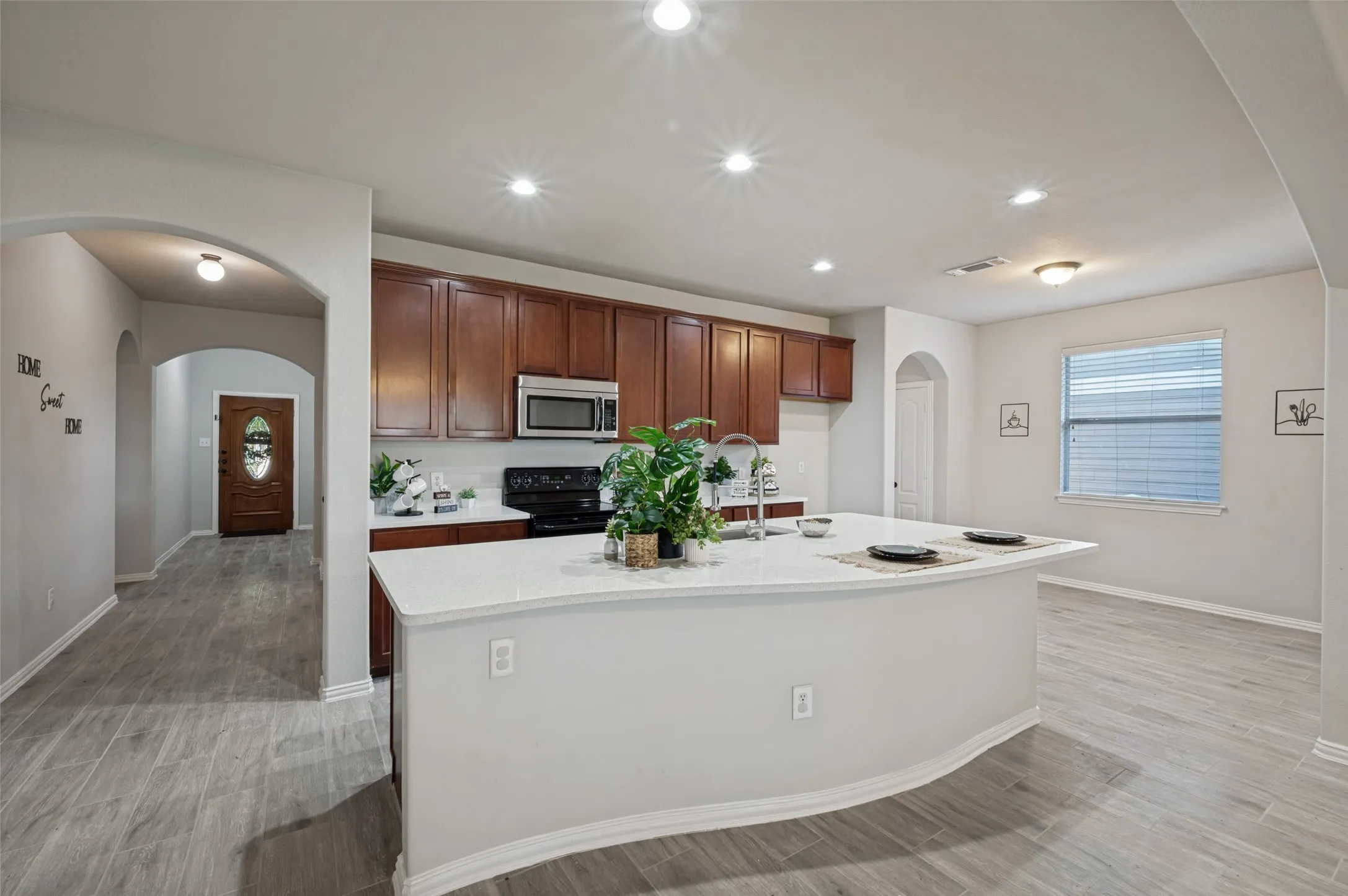 Open-concept kitchen featuring an eat-at island with a stainless steel sink, dark wood cabinetry, white countertops, and stainless steel appliances