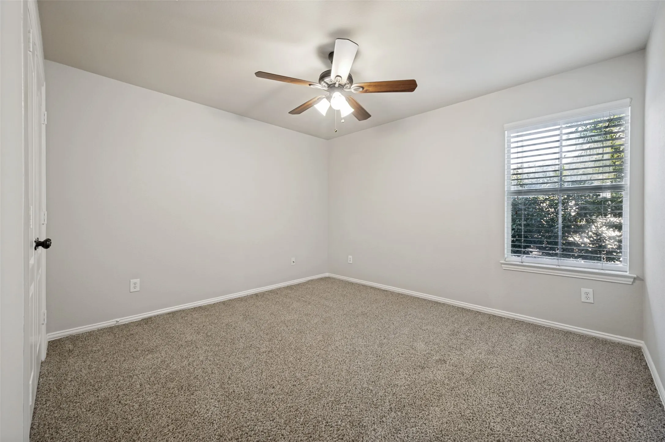 Carpeted room featuring a ceiling fan with integrated lighting, a window with horizontal blinds, and a white paneled door