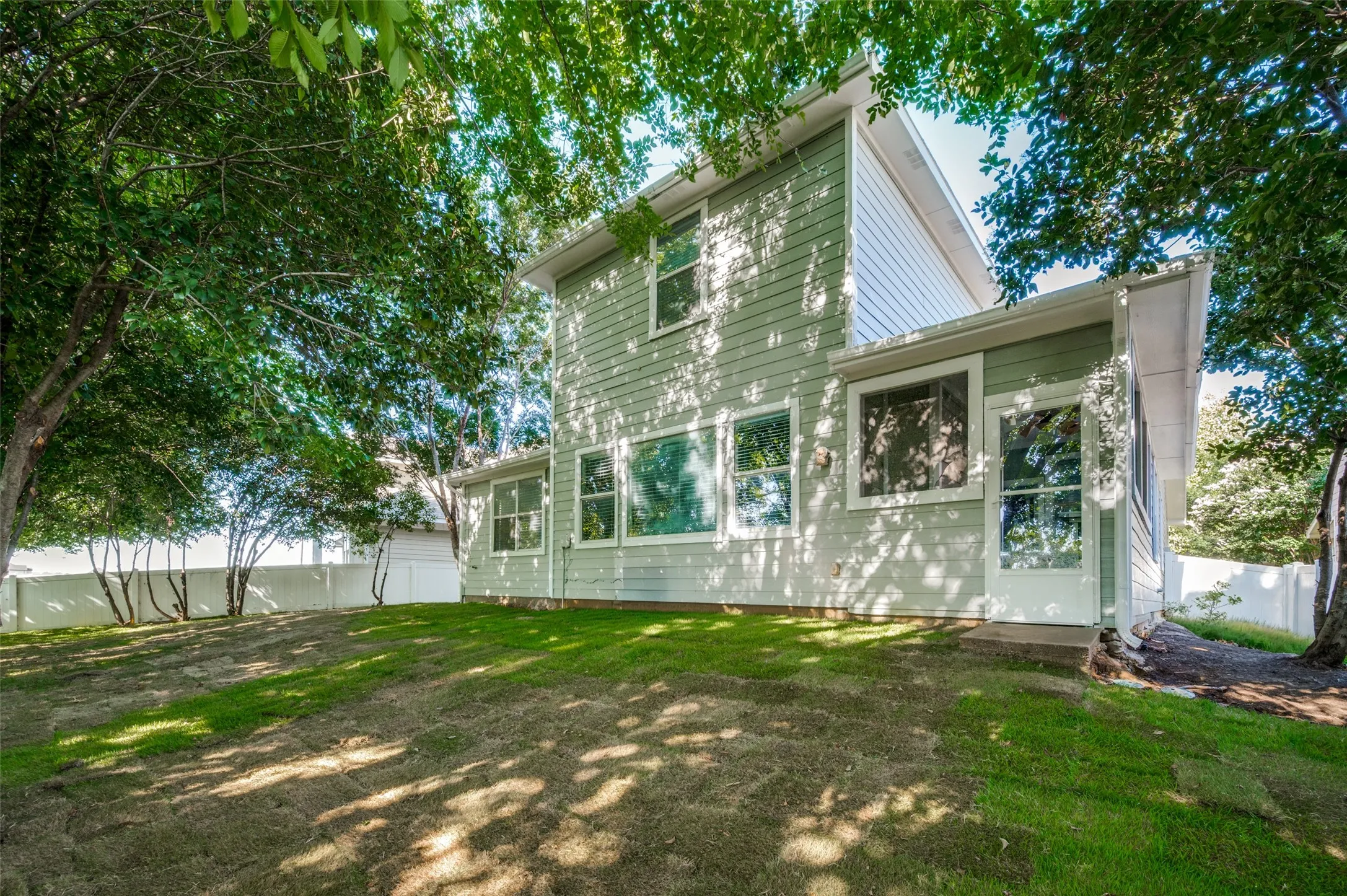 Expansive backyard featuring a green lawn, mature trees, and a white privacy fence