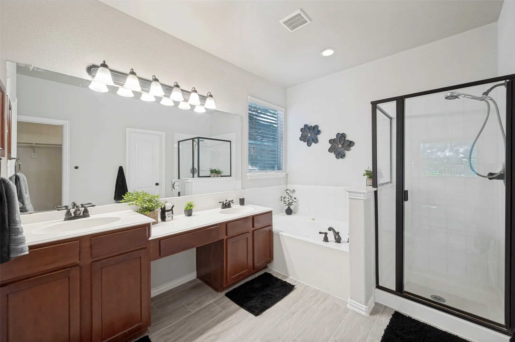 Spacious bathroom featuring a dual vanity with undermount sinks, warm wood cabinetry, a built-in soaking tub, a separate glass-enclosed shower, and wood-finish tile flooring
