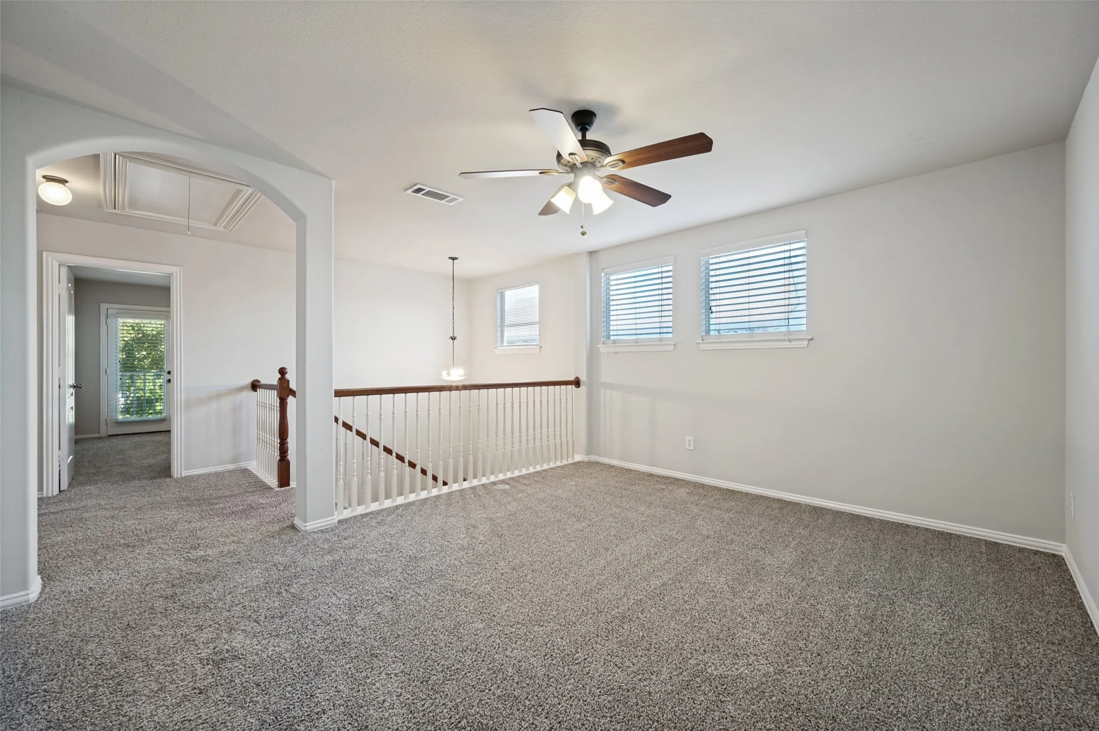 Carpeted interior space featuring an arched entryway, white baluster railing with wood-finish top rail, and a ceiling fan