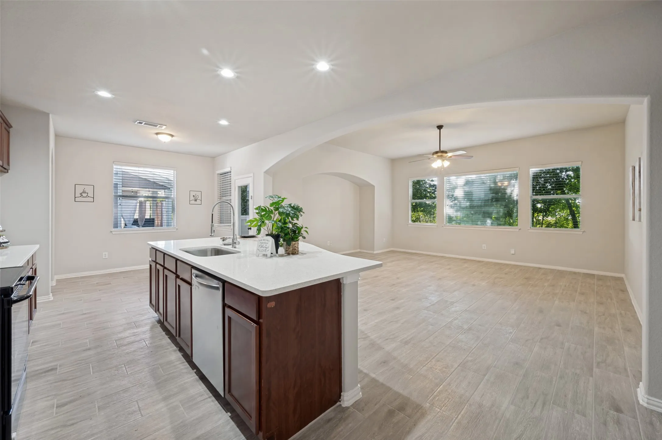 Open-concept kitchen and living area featuring wood-finish flooring, a kitchen island with built-in cabinetry and an undermount sink, recessed lighting, and large windows