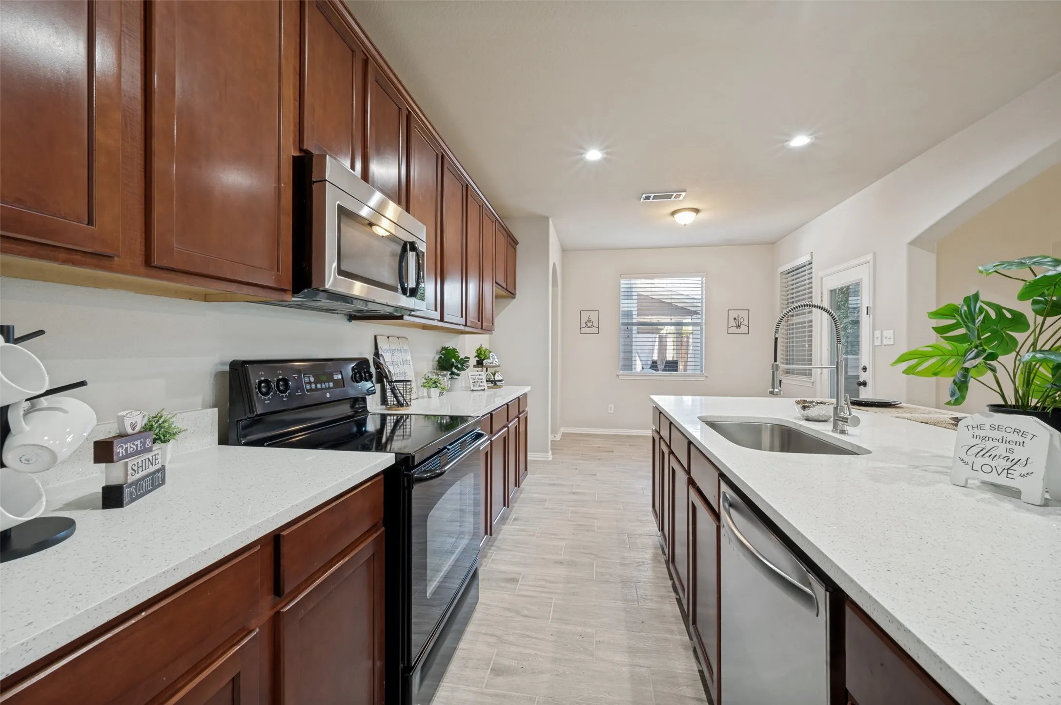 Modern kitchen featuring wood-finish cabinetry, light stone-look countertops, stainless steel appliances, and wood-finish flooring