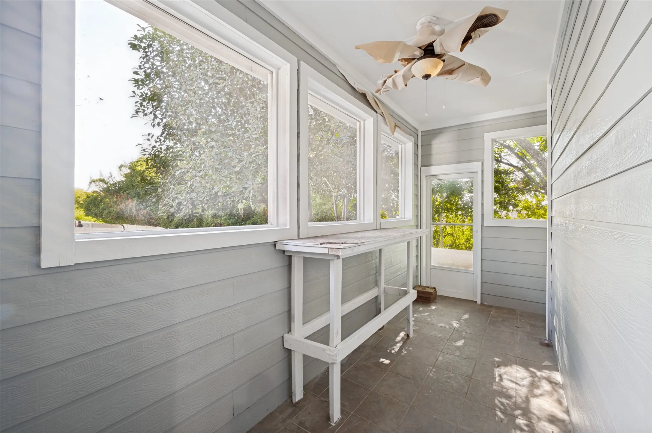 Sunroom with three large windows, gray horizontal paneling, and tiled flooring