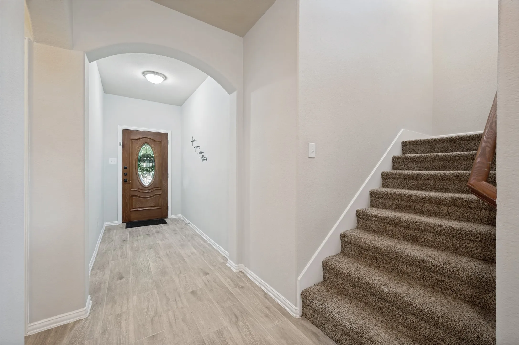 Entryway featuring a wood-panel door with an oval glass insert, an arched doorway, wood-finish flooring, and a carpeted staircase with a wood handrail