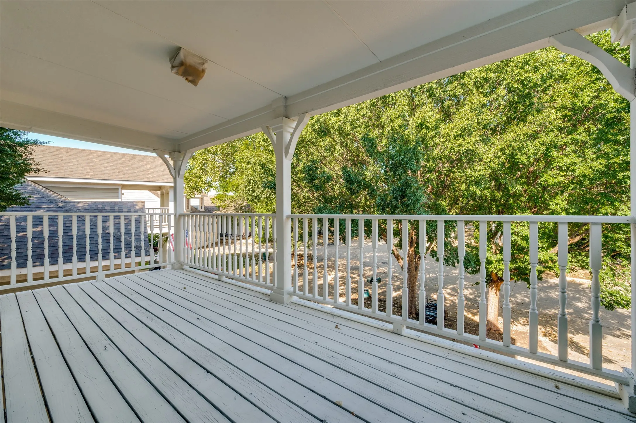Covered outdoor balcony featuring white painted wood flooring and baluster railing
