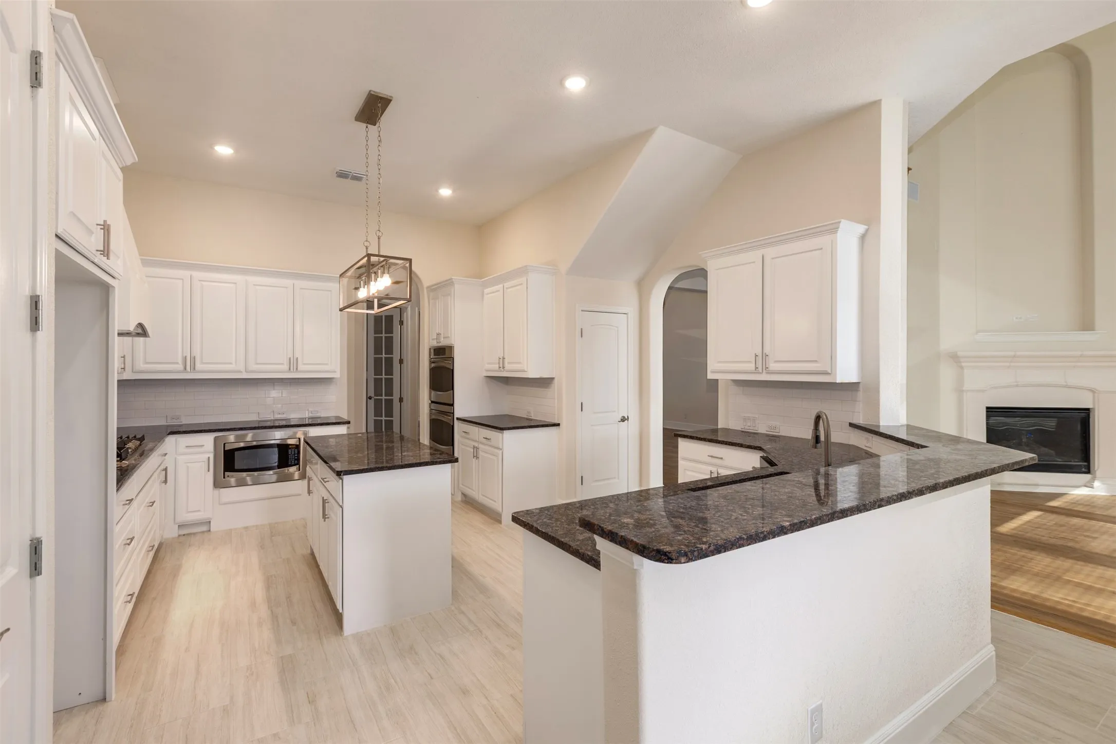 Kitchen featuring white cabinets, a peninsula, a center island, light wood finished floors.