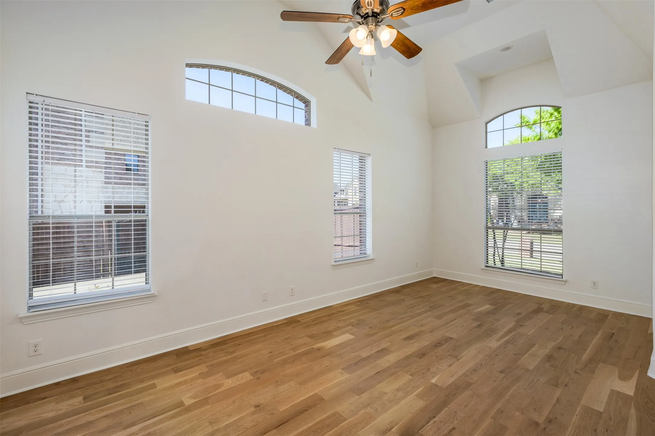 Primary bedwith wood finished floors, a ceiling fan, a high ceiling, and plenty of natural light